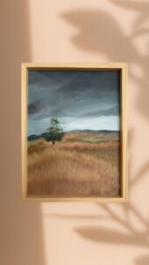 Obraz przedstawiający rozległe, złociste pola pod ciężkim, grafitowym niebem. Samotne drzewo na pierwszym planie jest symbolem trwania w otwartej, burzliwej  przestrzeni.