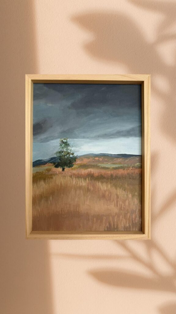 Obraz przedstawiający rozległe, złociste pola pod ciężkim, grafitowym niebem. Samotne drzewo na pierwszym planie jest symbolem trwania w otwartej, burzliwej  przestrzeni.