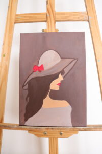 Kobieca sylwetka uchwycona w półprofilu. Kontrast ciemnych włosów  z akcentem czerwieni nadaje kompozycji wyrazistości i elegancji.